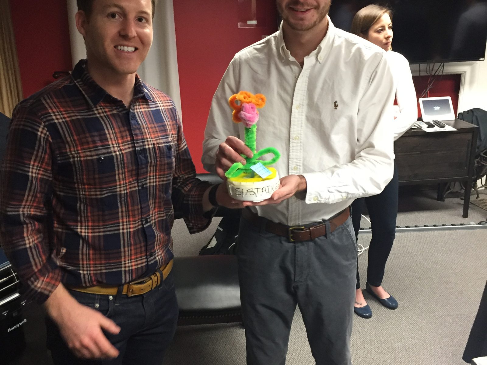 Two Motivf team members holding a flower sculpture made from colorful pipe cleaners, with a colleague in the background.