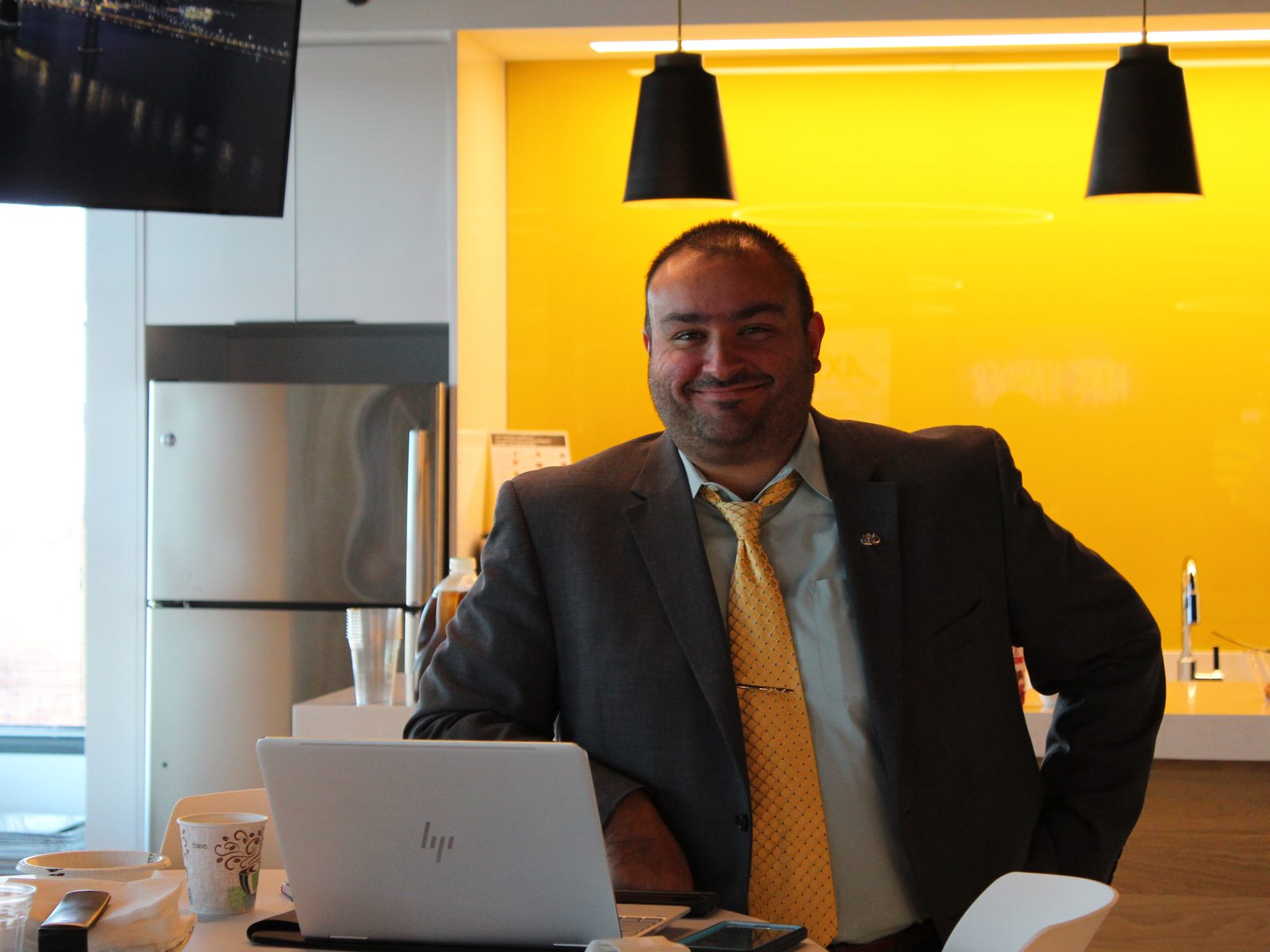 A Motivf team member standing in a bright office kitchen with a yellow wall, smiling.